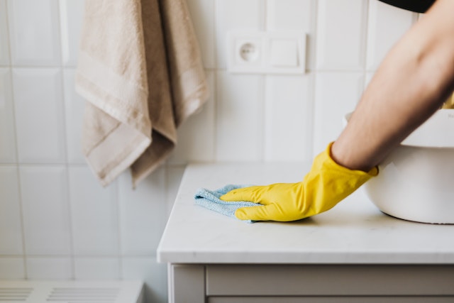 someone wearing a yellow gloves wiping down a bathroom counter